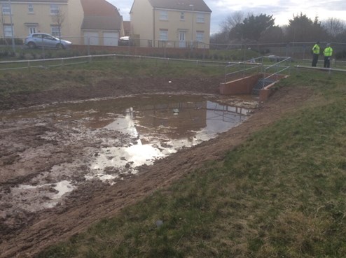 Large grassy basin in new housing development. Eroded banks of basin.