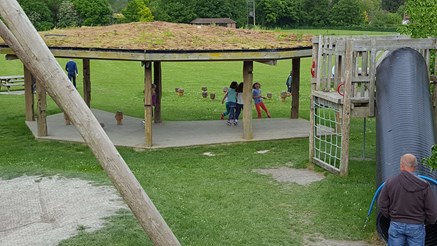 Playground with slide and children playing. Wooden covered play area has a green roof