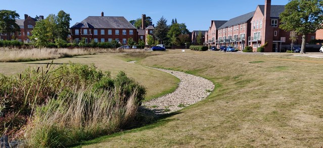 Houses overlooking gravel-lined swale leading to grassy basin