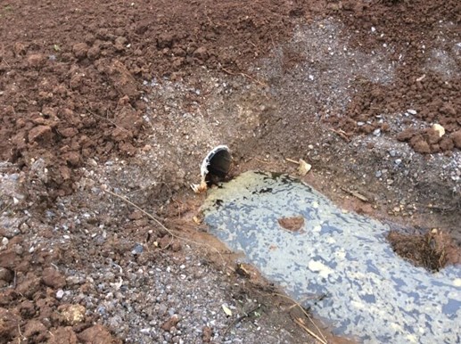 Pipe in earth mound with stagnant water